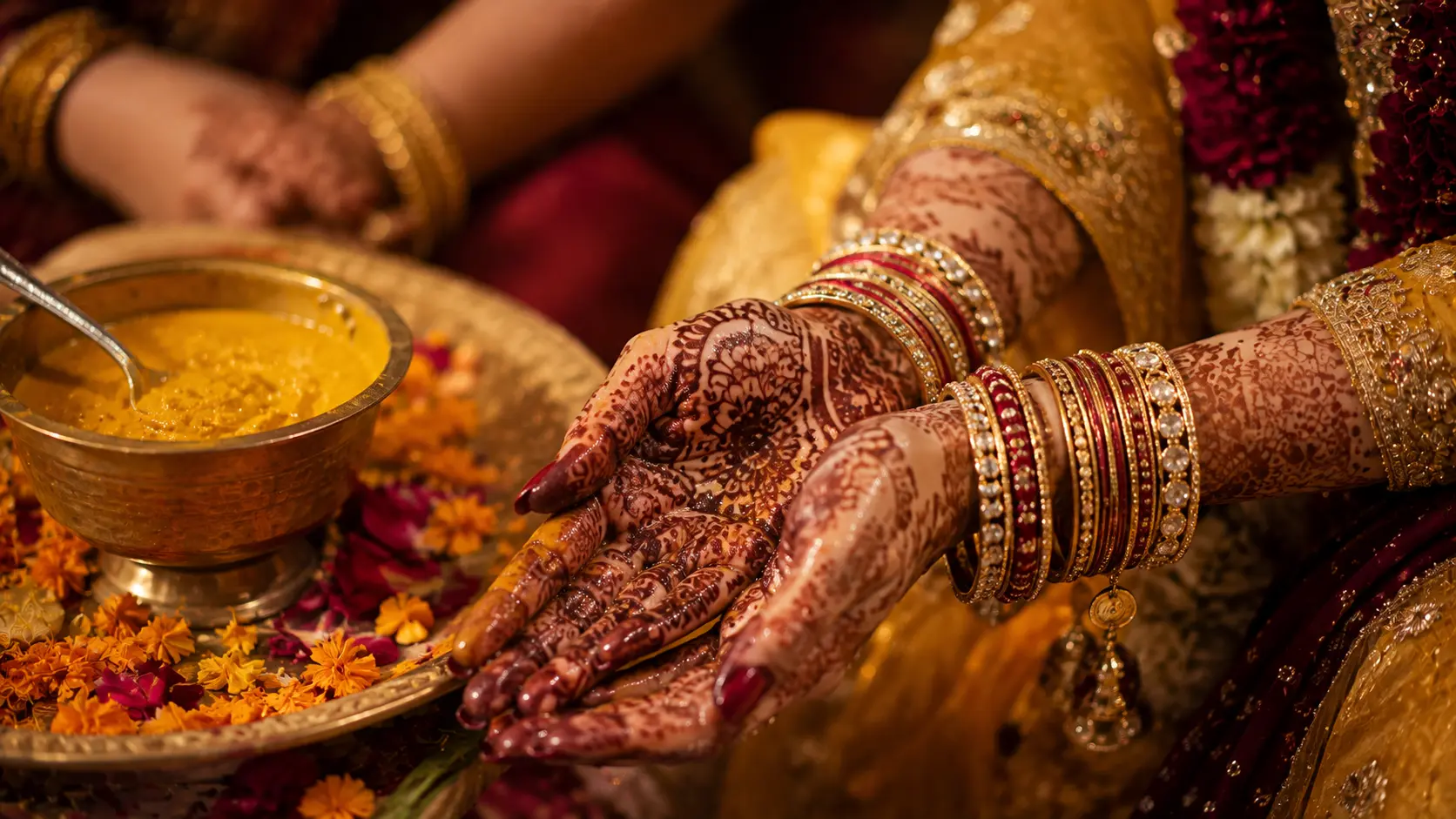Bride's hands decorated with mehendi beside turmeric paste and marigold petals